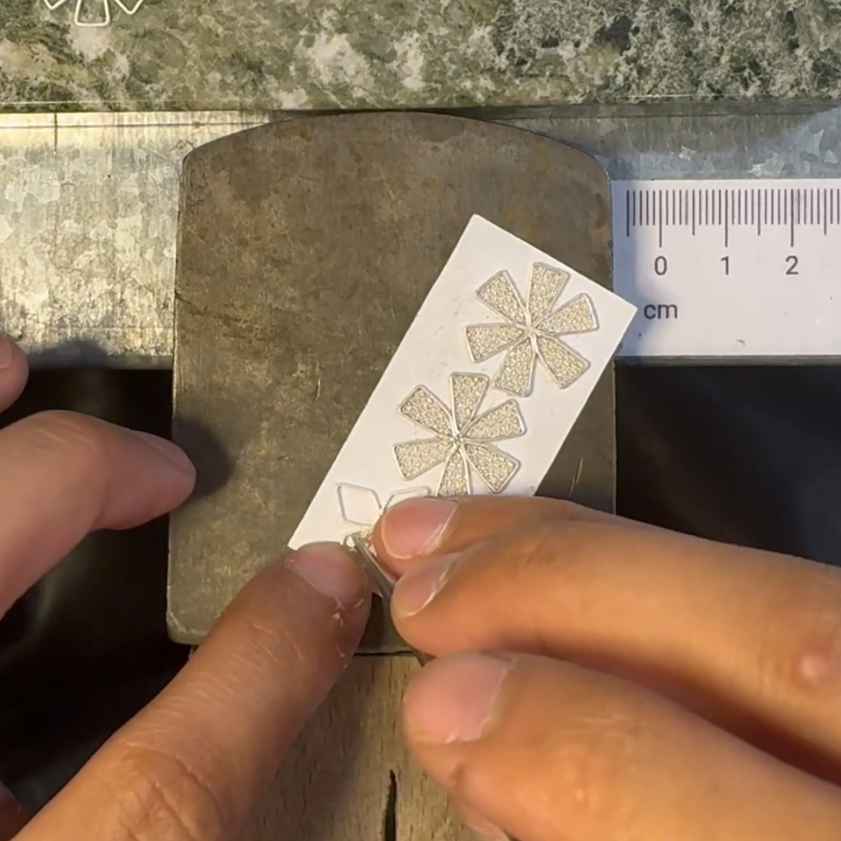 A jeweller's benchpeg and two hands inserting filigree wire into flower-shaped frames