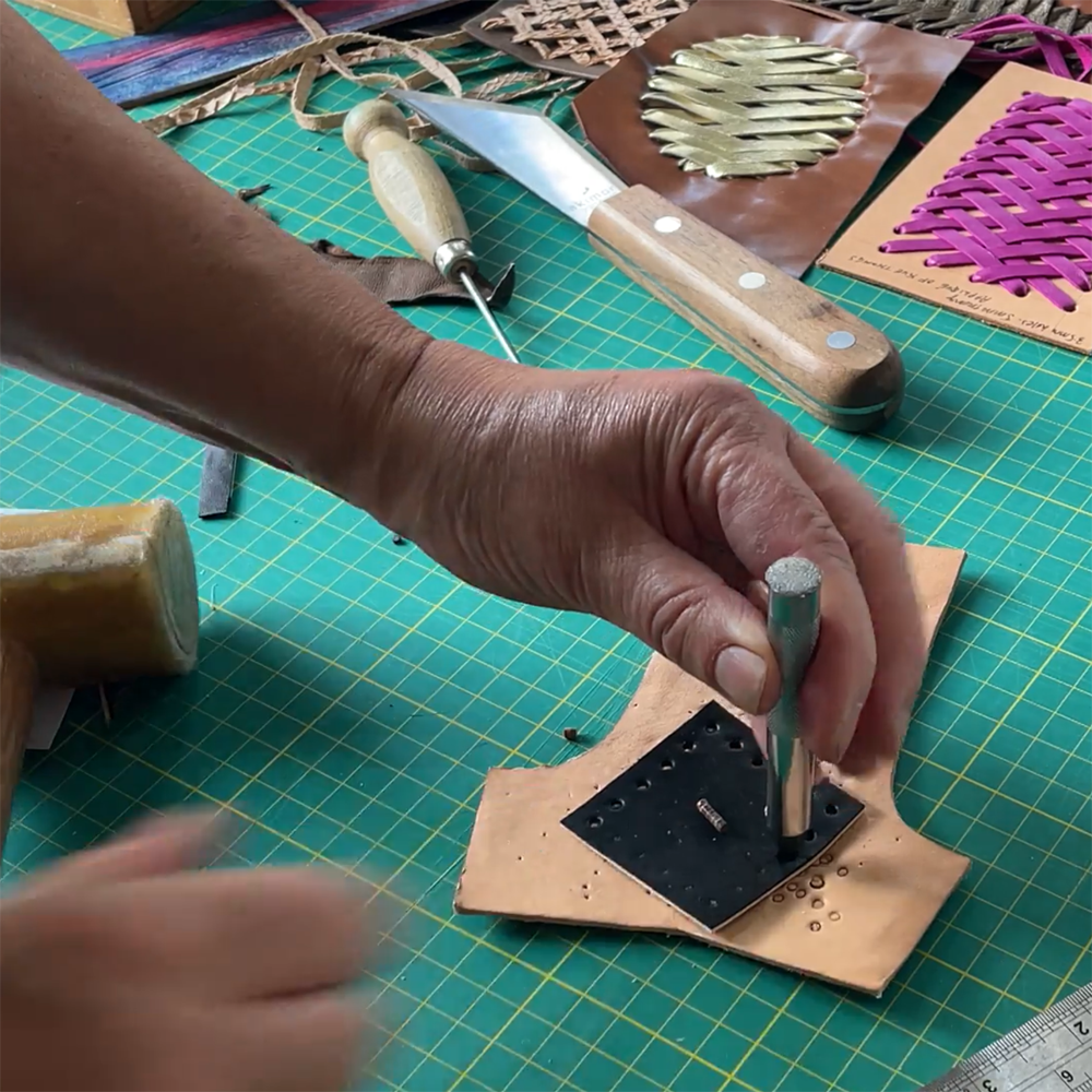 Heather Blake working with leather to create jewellery on a green cutting mat with tools.