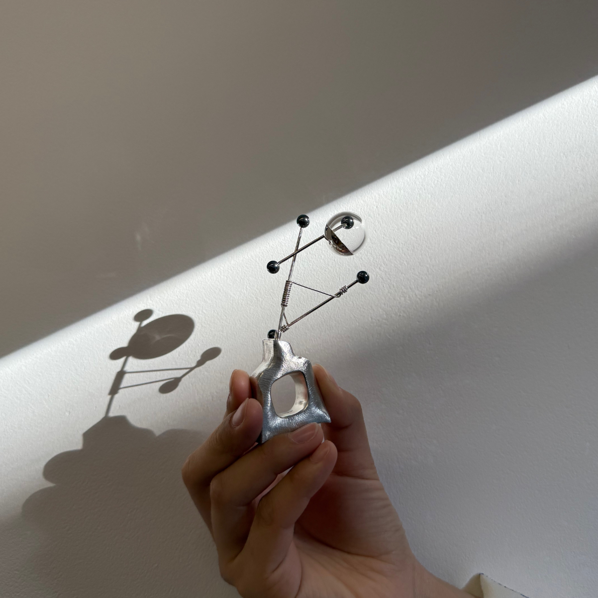 Hand holding a unique silver ring by Wenyin Jiang against a light background